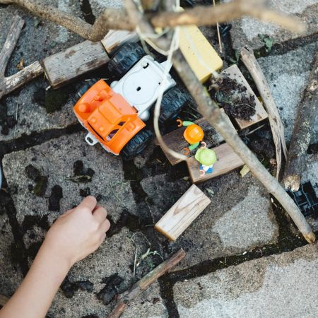 Ein Kind spielt mit Bauspielzeug und Holzstöcken auf dem Boden, während es kreative Konstruktionen gestaltet.
