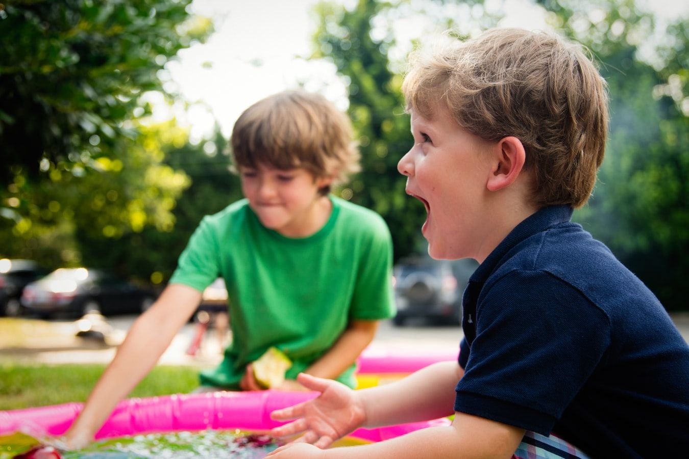 Zwei fröhliche Kinder spielen im Wasser eines Planschbeckens und genießen einen sonnigen Tag im Freien.
