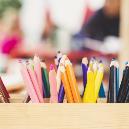 Ein Holzkasten voller Buntstifte in verschiedenen Farben steht auf einem Tisch, bereit zum Zeichnen und Malen.