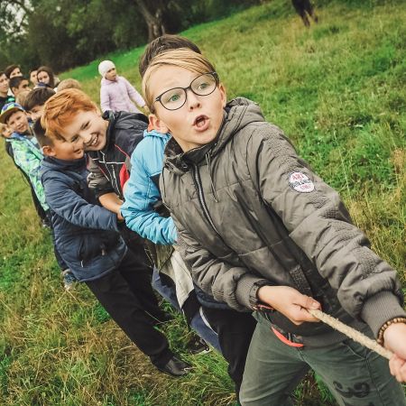 Eine Gruppe von Kindern zieht gespannt an einem Seil in einem grünen Feld während eines fröhlichen Spiels.