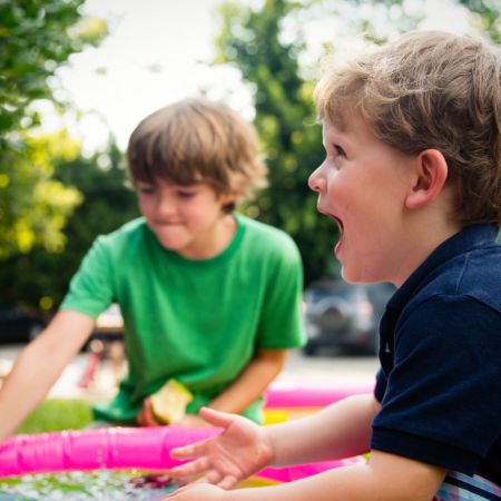 Zwei fröhliche Kinder spielen im Wasser eines Planschbeckens und genießen einen sonnigen Tag im Freien.